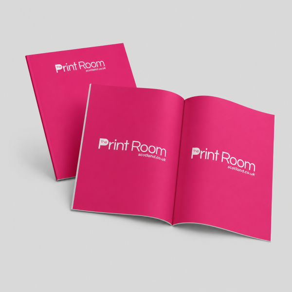 Stack of pink Print Room perfect bound brochures with white logo branding on a light grey studio background.