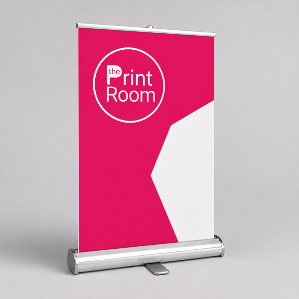 Desktop roll-up banner featuring The Print Room round magenta logo, a modern pink and white geometric design, and a compact aluminium retractable banner stand on a neutral studio background.