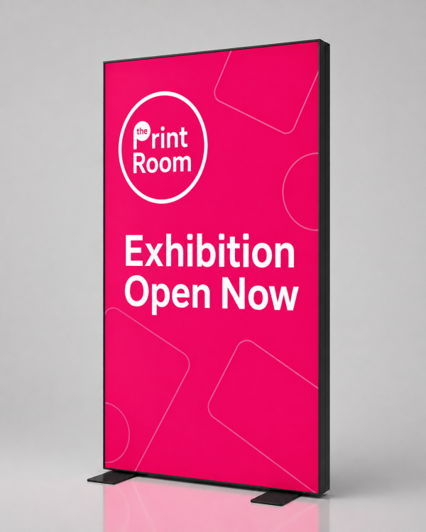 Freestanding LED lightbox display featuring The Print Room round magenta logo, the message "Exhibition Open Now," a vibrant illuminated pink display panel, and a slim black frame on a neutral grey studio background.