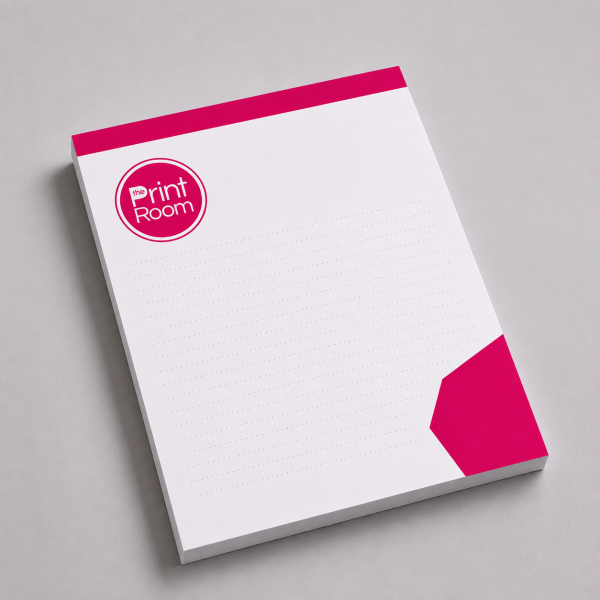 Custom printed notepad featuring the Print Room circular logo, with a white writing area, pink header and corner accent, displayed on a light grey studio background.