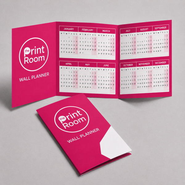 Folded wall planner with the Print Room circular logo, shown open and closed on a light grey studio background, featuring a full year calendar layout in a vibrant pink branded design.