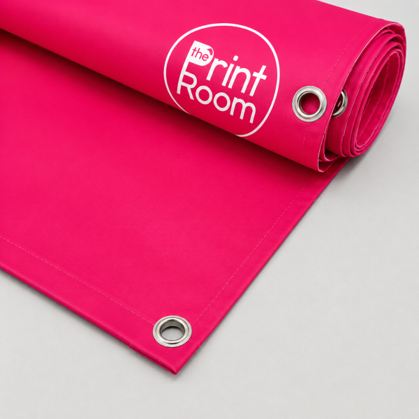 Rolled single sided PVC banner in The Print Room branding with hemmed edges and metal eyelets, shown partially unrolled on a light grey background.