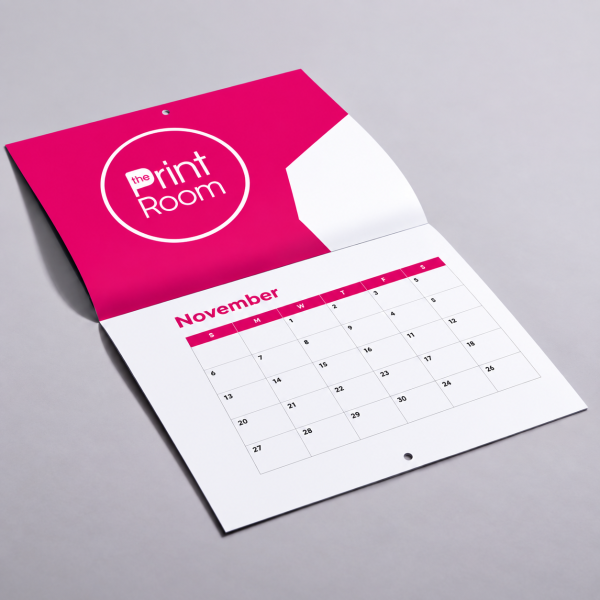 Open November wall calendar featuring The Print Room round magenta logo, a modern pink and white geometric design, and a monthly date grid displayed on a clean tabletop mockup.